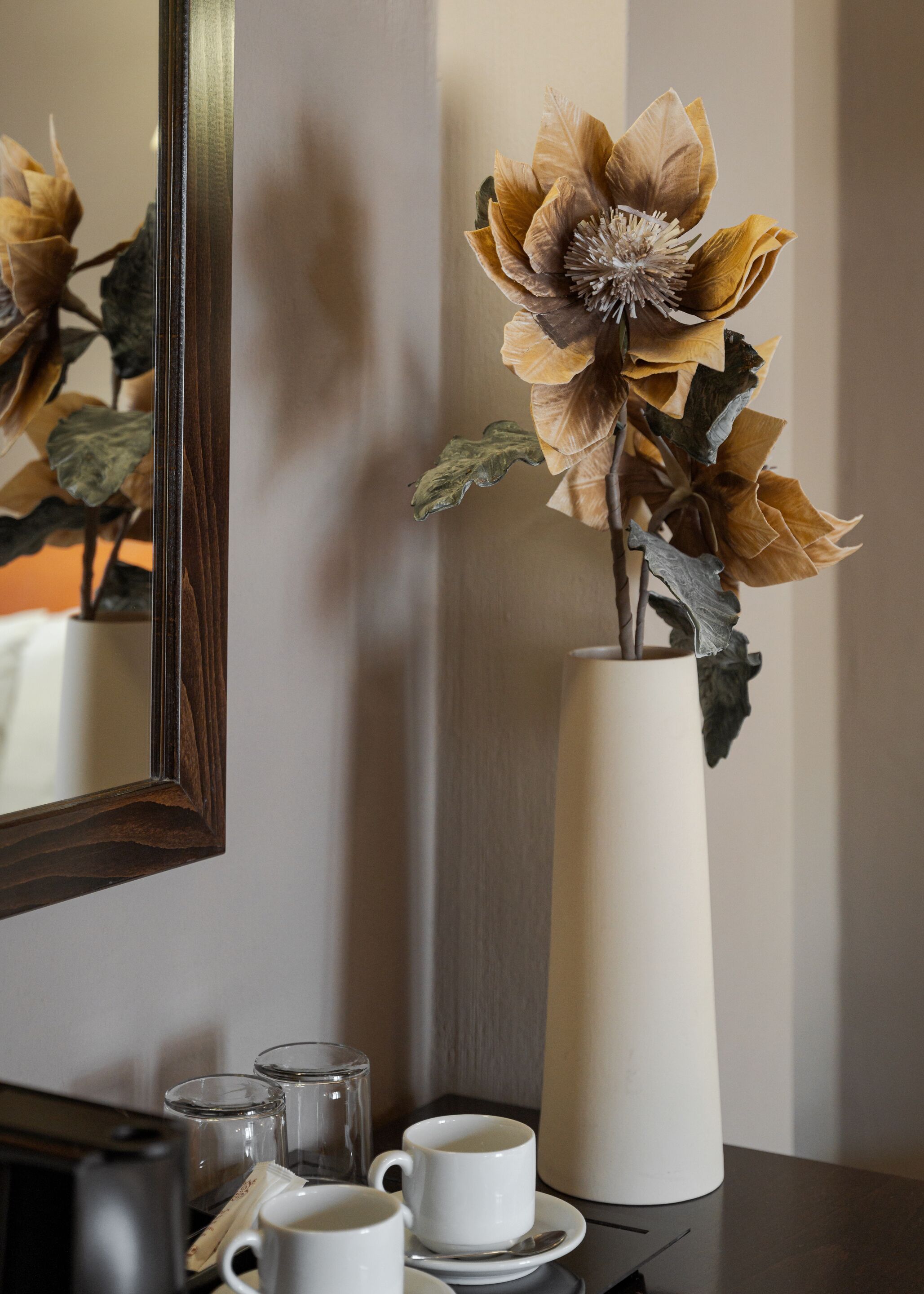 A vase with dried flowers on a table next to a mirror.