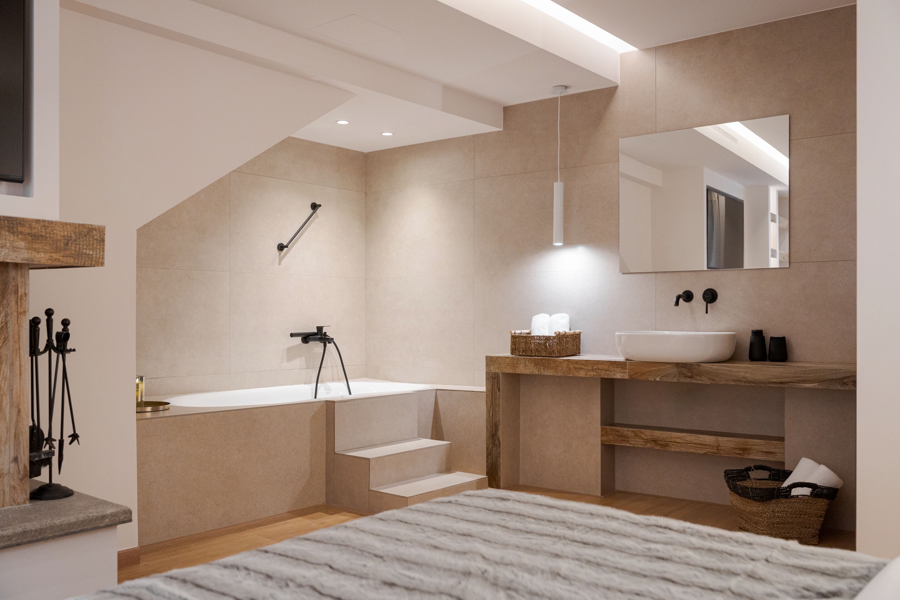 Une salle de bain moderne avec une baignoire, un lavabo et un miroir. Des marches mènent à la baignoire, et une étagère en bois contient des articles de toilette.