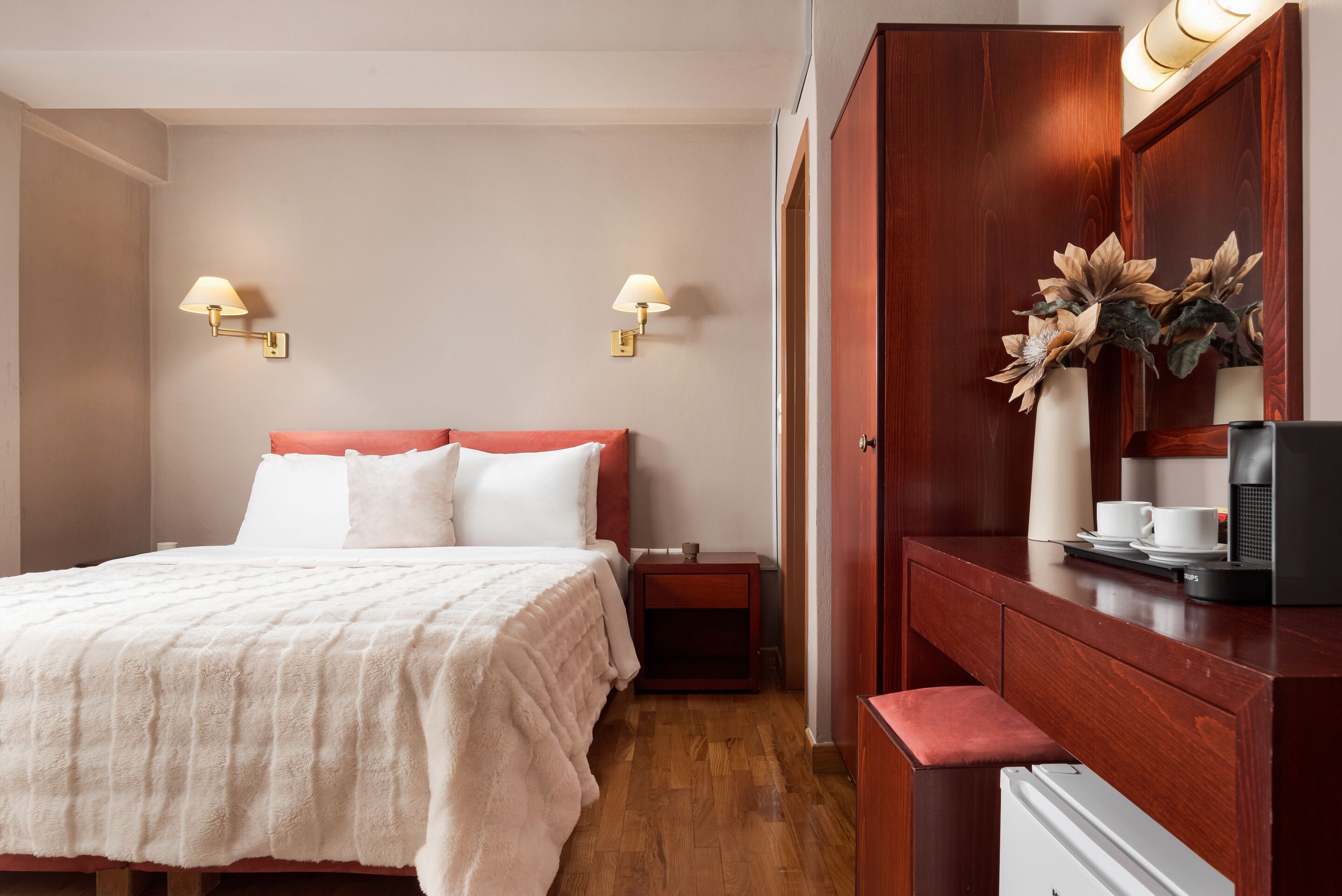 A hotel room with a bed, bedside tables, a desk with a coffee maker, and wall-mounted lamps.