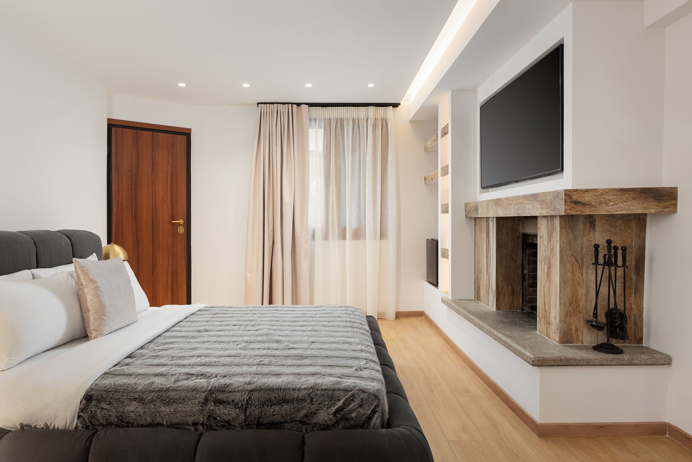 A modern bedroom with a bed, a TV mounted above a fireplace, and a door.