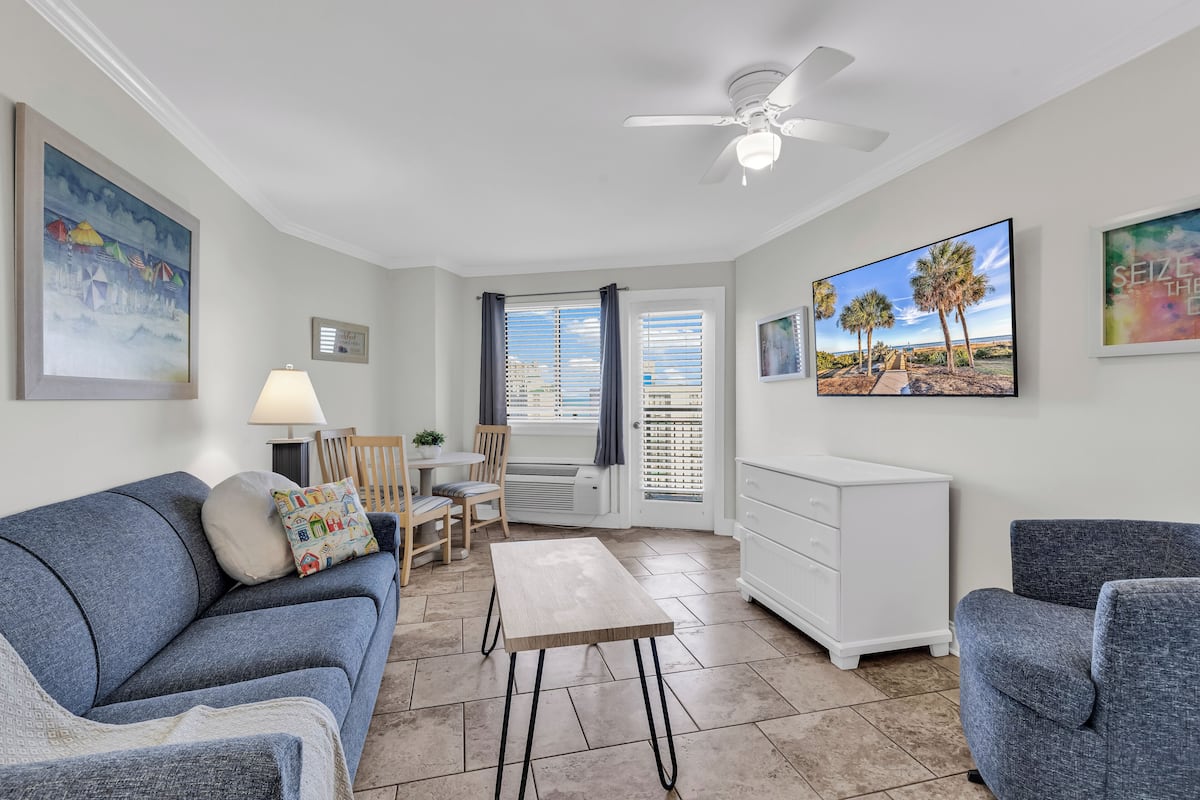 A living room with a blue sofa, a wooden coffee table, a white dresser, and a ceiling fan.