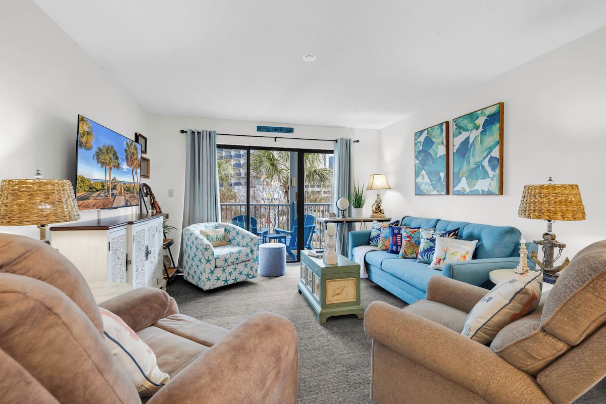 A living room with a sofa, armchairs, a TV, and a balcony with a view.
