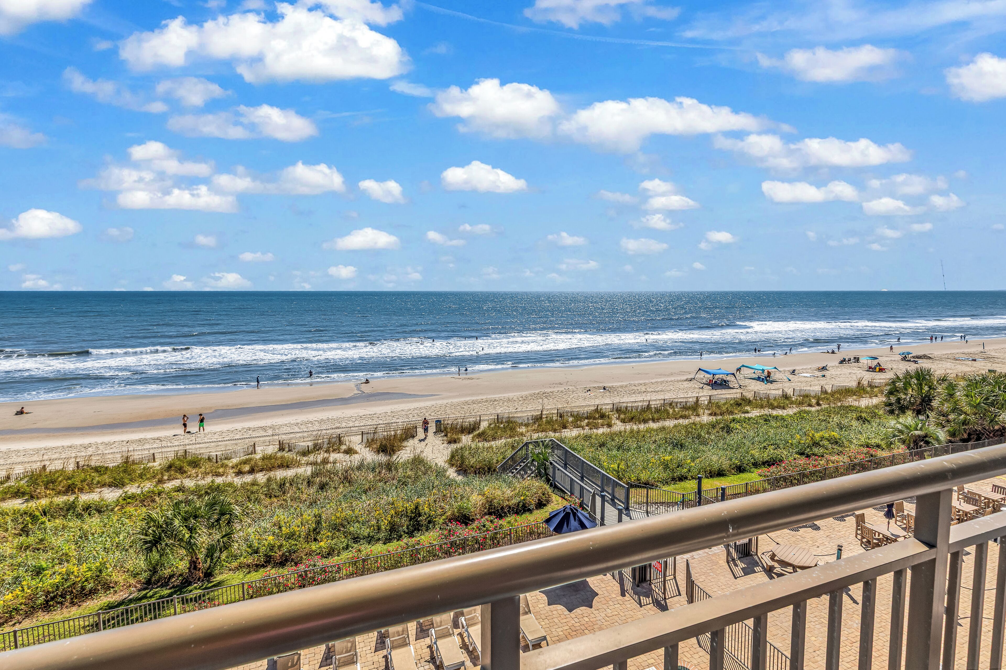 A beach view from a balcony with a railing, a sandy beach, and the ocean.