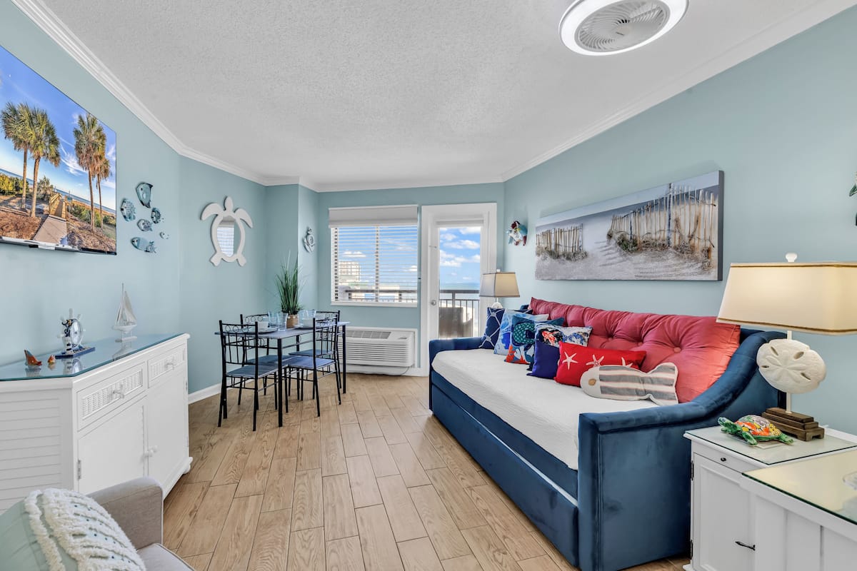A room with a blue sofa, a dining table, and a white cabinet.