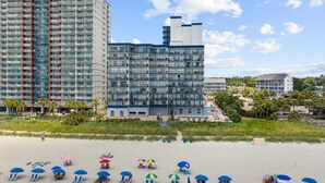 A beachfront hotel with multiple floors, a pool, and beach umbrellas.