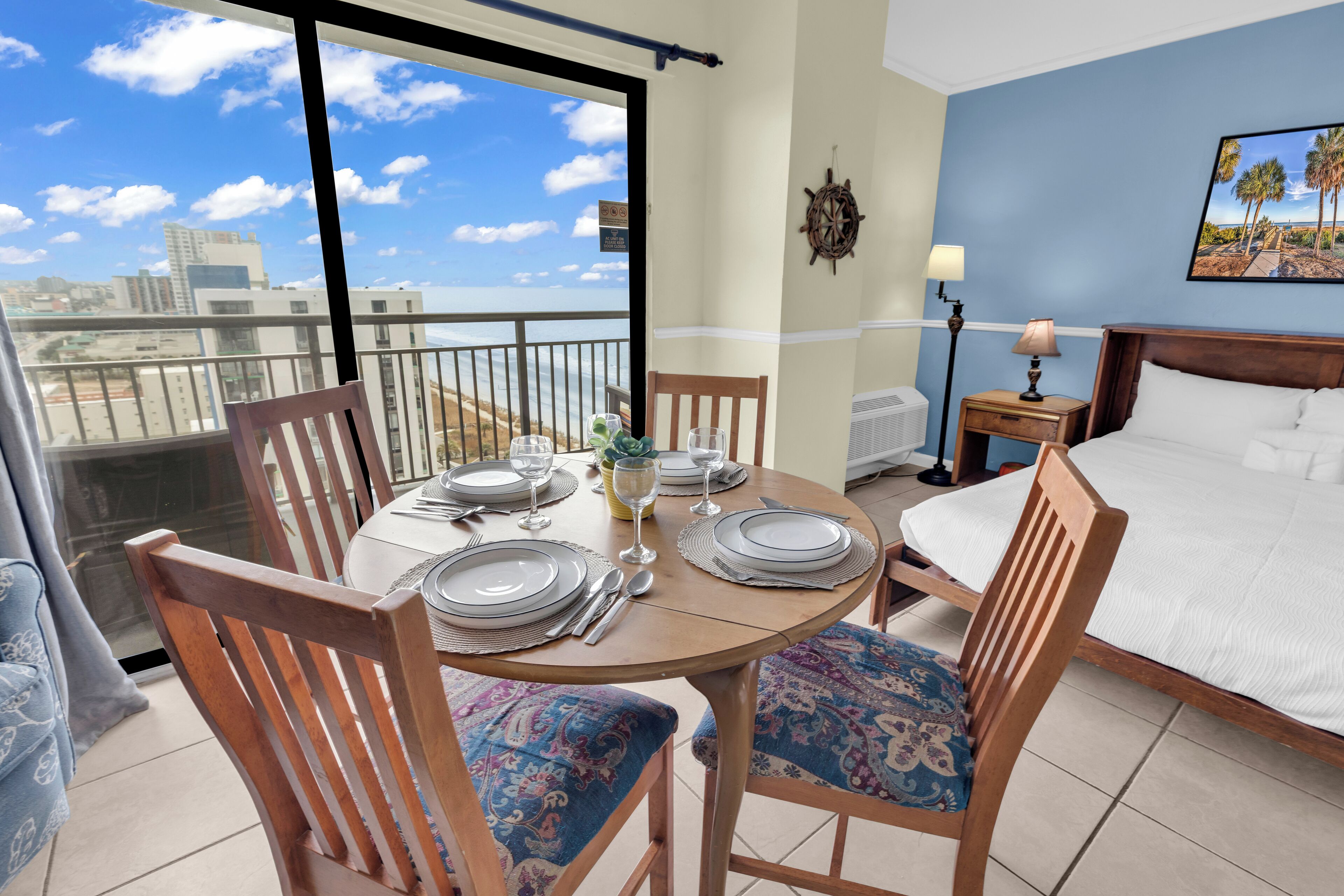 Une chambre d’hôtel avec un balcon, une table à manger dressée pour quatre personnes, un lit et une vue sur les toits de la ville.