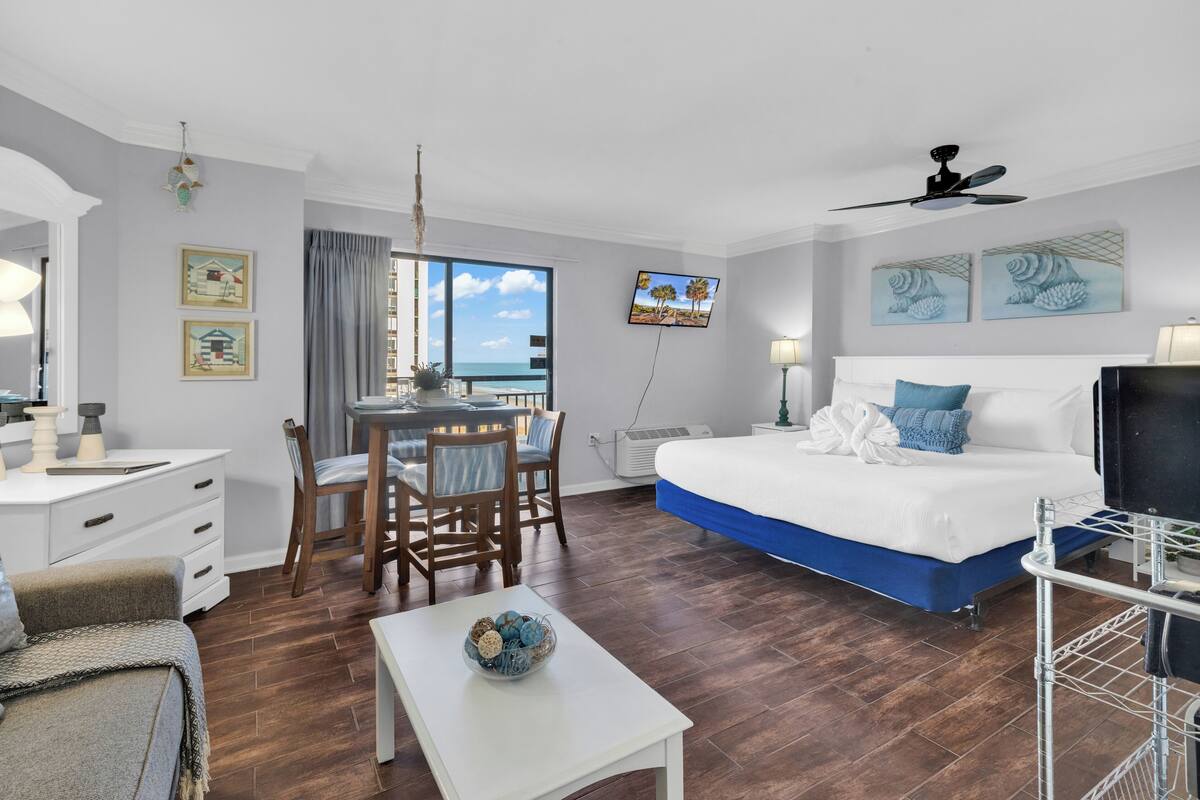 A hotel room with a bed, a desk, a dining table, and a TV.