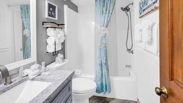 Une salle de bain avec un lavabo, des toilettes et une baignoire, tous de couleur blanche. On y trouve des serviettes et des articles de toilette sur le comptoir.