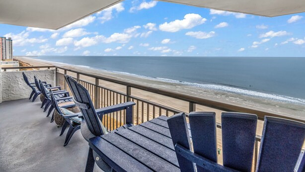 A balcony with chairs overlooking a beach and ocean.