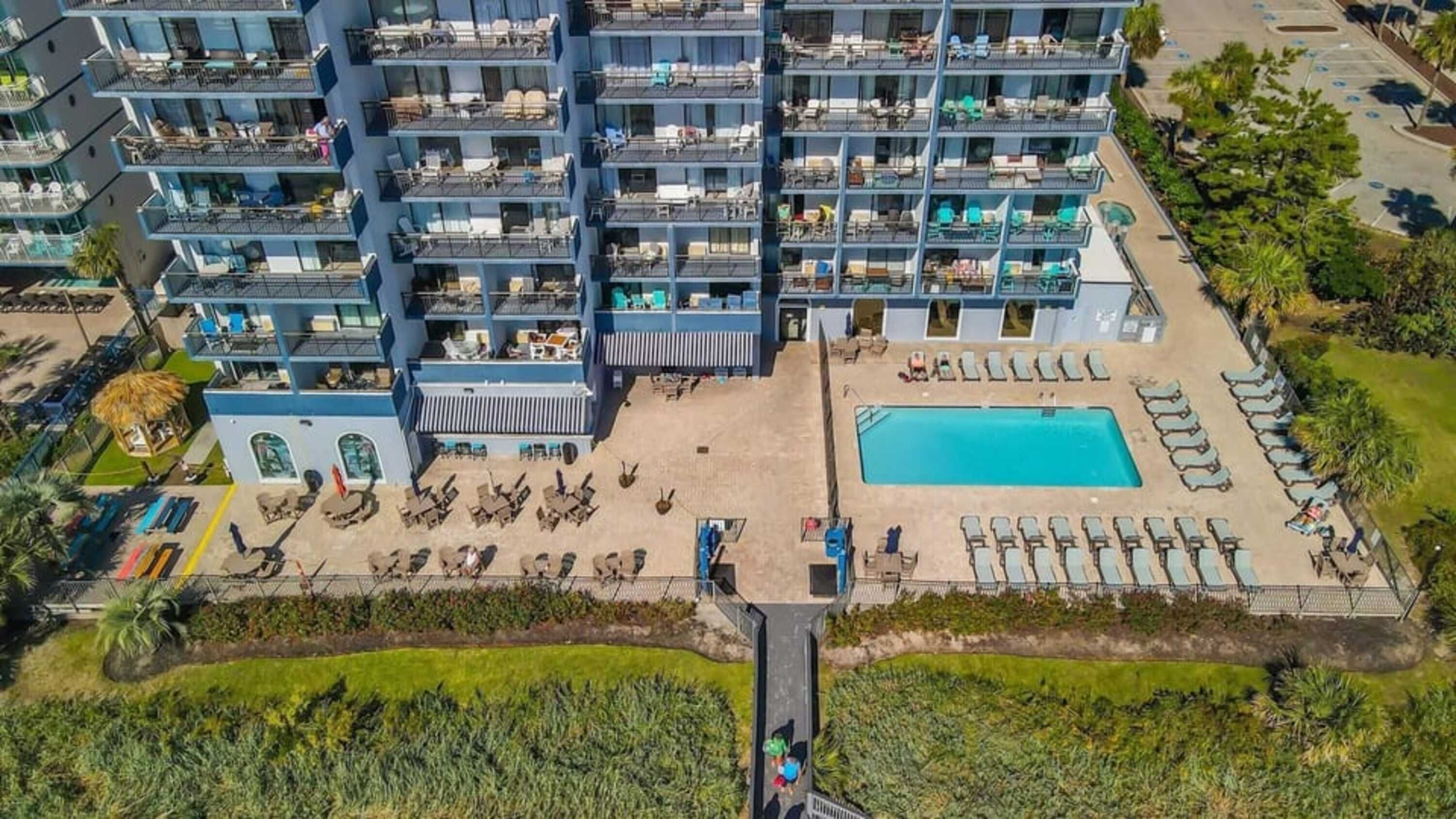Un hotel de varios pisos con balcones, piscina y zonas de estar al aire libre.