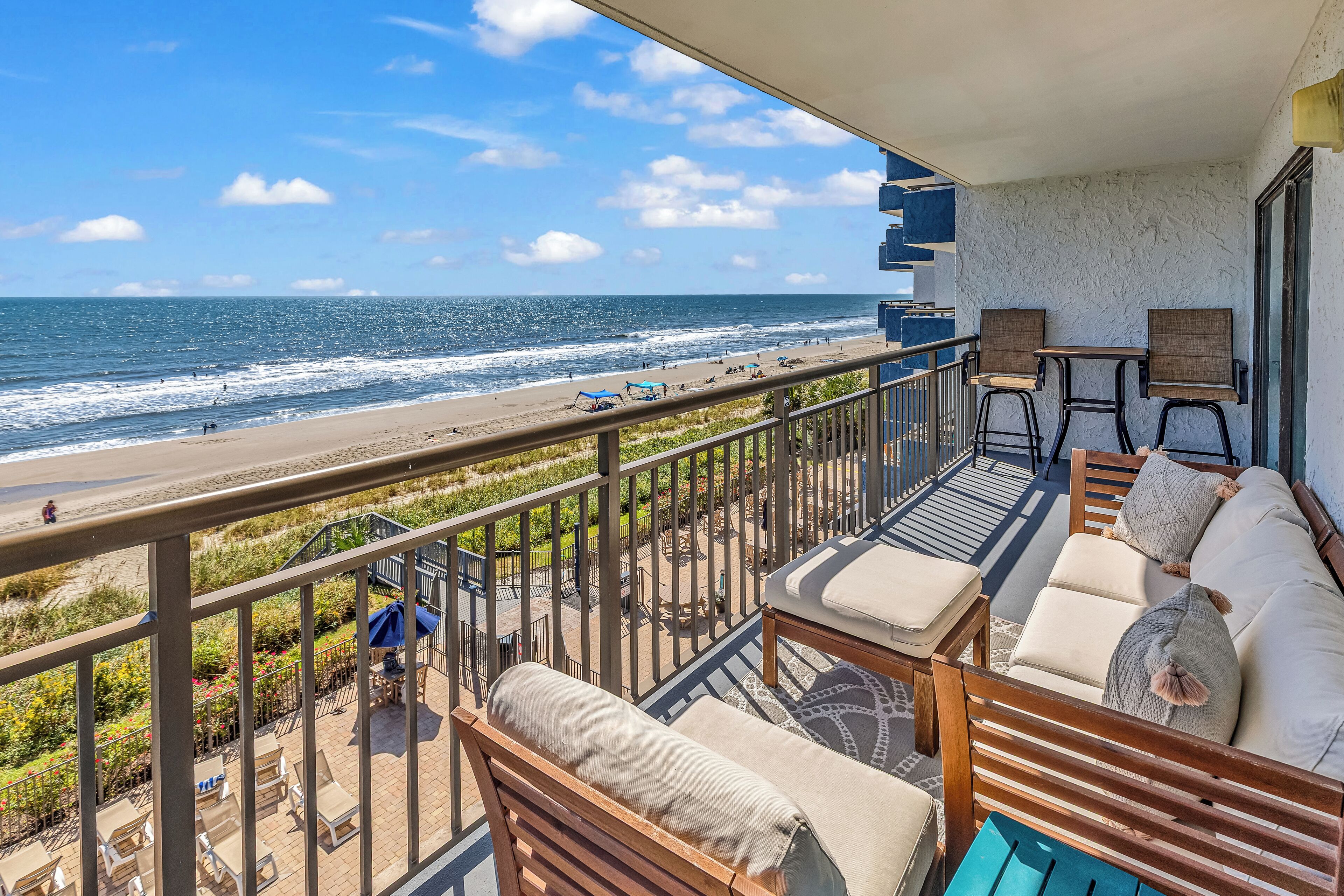 A balcony with a view of the beach and ocean, furnished with a sofa and chairs, and a small table.