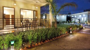 Un hotel moderno con una zona de estar al aire libre techada, una entrada bien iluminada y un jardín ajardinado.