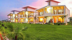 Una casa moderna de varios pisos con amplios ventanales y balcones, rodeada de un césped cuidado y palmeras.