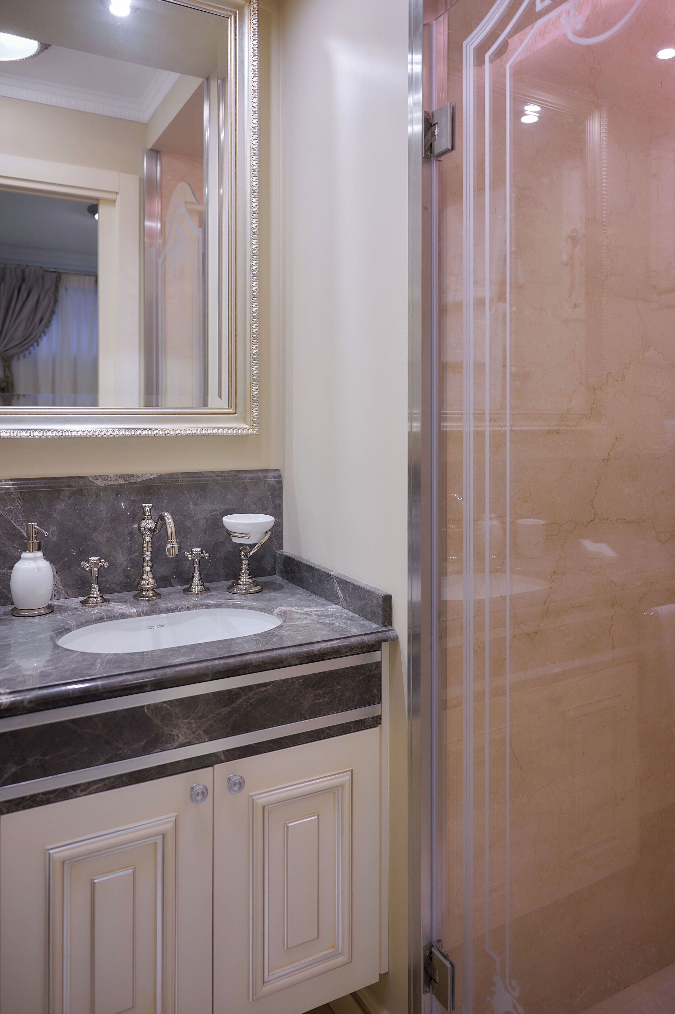 Une salle de bain avec un comptoir en marbre, un lavabo, un miroir et une douche à parois de verre.