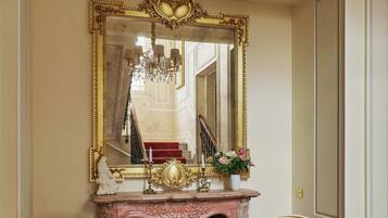 A room with a grand mirror, two ornate chairs, a fireplace, and a chandelier.