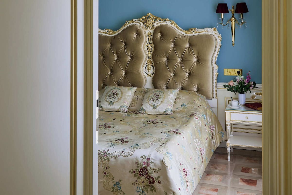 Une chambre à coucher avec un grand lit à baldaquin décoré, un lustre et une table de chevet avec une lampe.