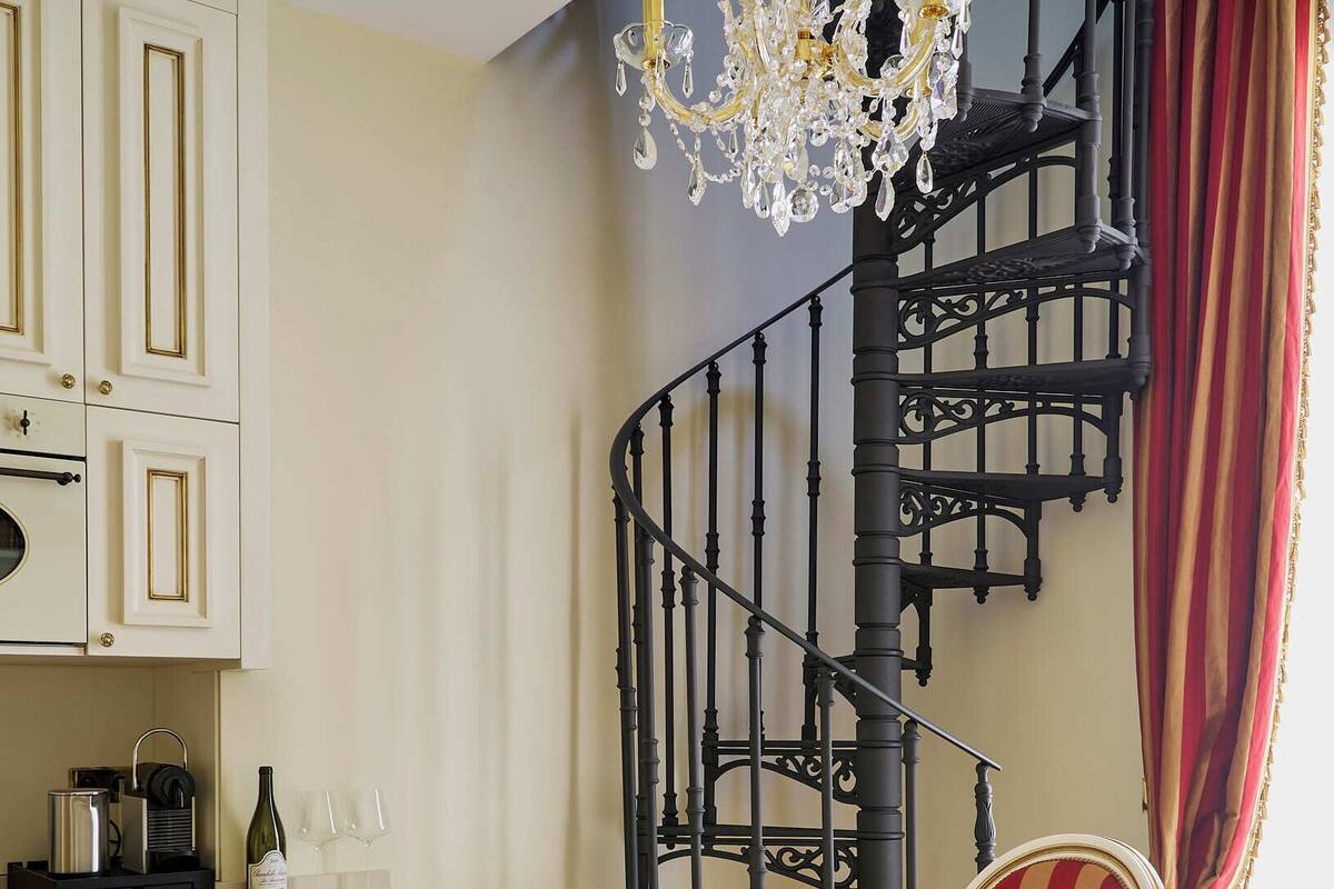 Un espace repas comprenant une table blanche, deux chaises rouges à revêtement en tissu, un lustre et un escalier en colimaçon noir.