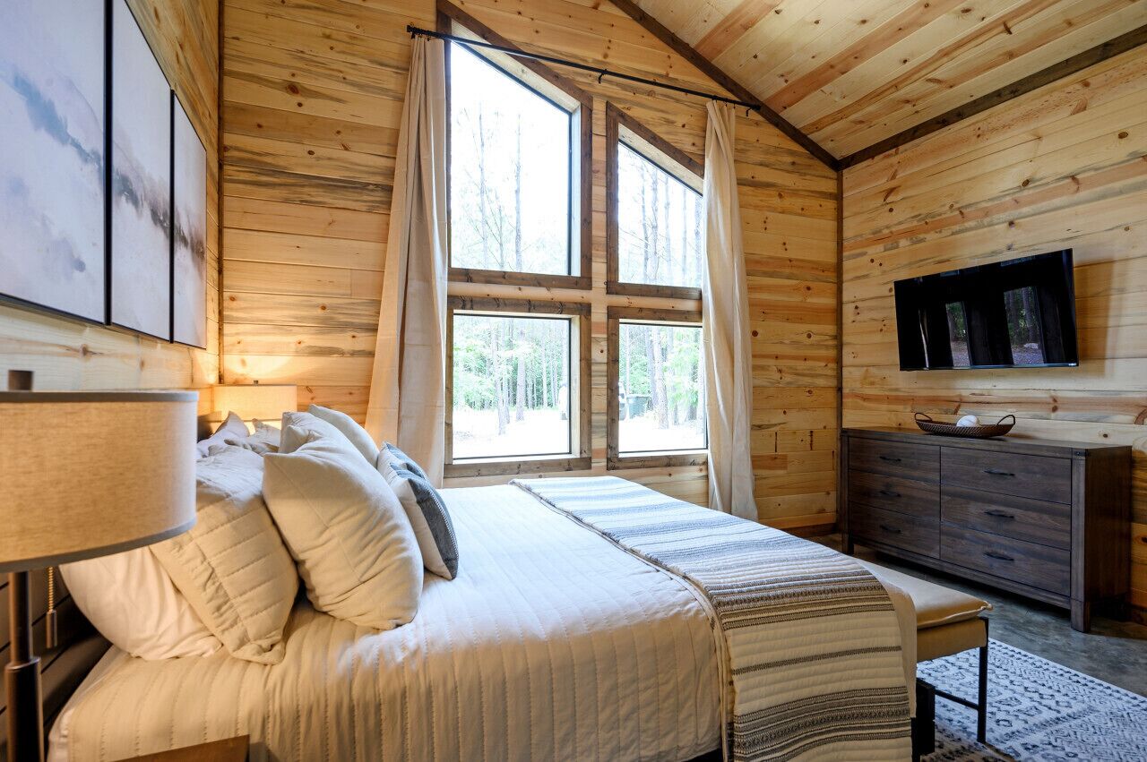 Ein Schlafzimmer einer Holzhütte mit einem Bett, einem Schminktisch und einem Fernseher an der Wand.
