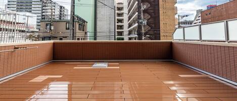 A spacious balcony with a tiled floor, overlooking a cityscape with various buildings and a clear sky.