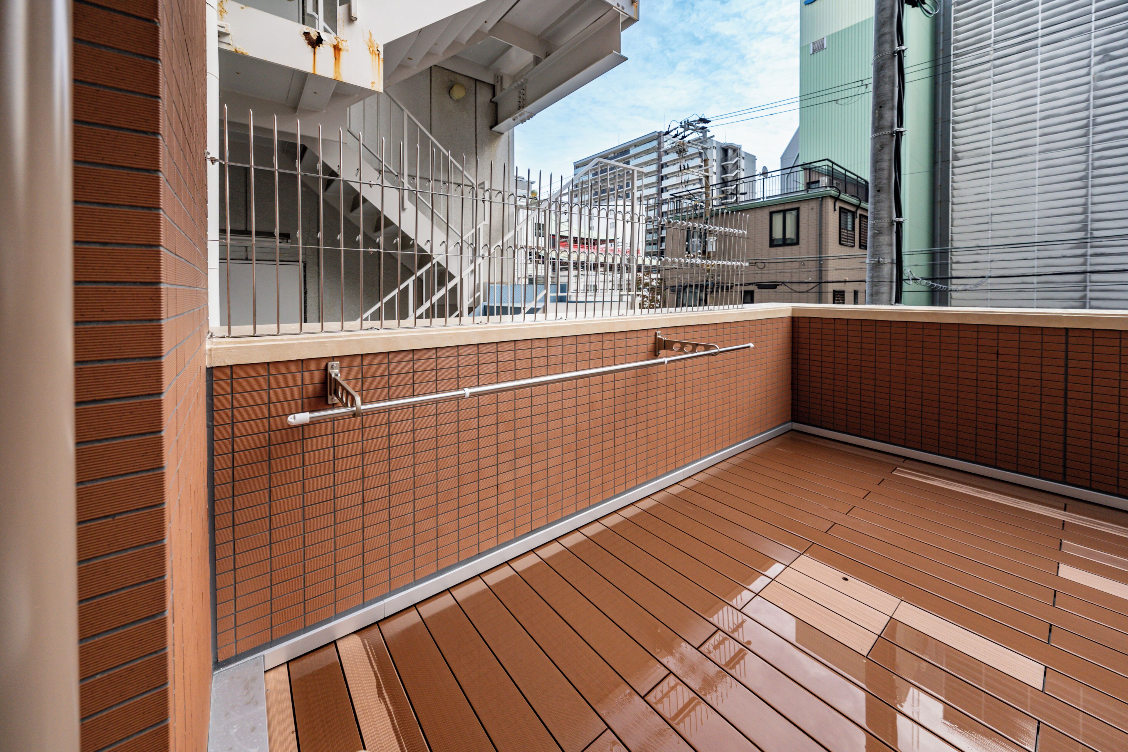 A balcony with a metal railing, wooden floor, and a view of buildings in the background.