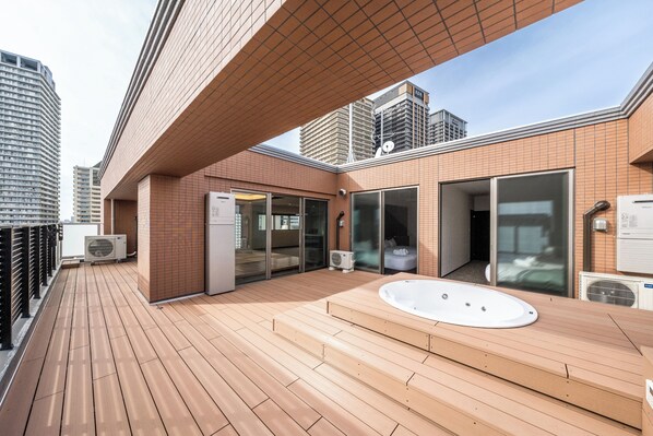 A rooftop terrace with a wooden deck, a hot tub, and a glass-enclosed room.