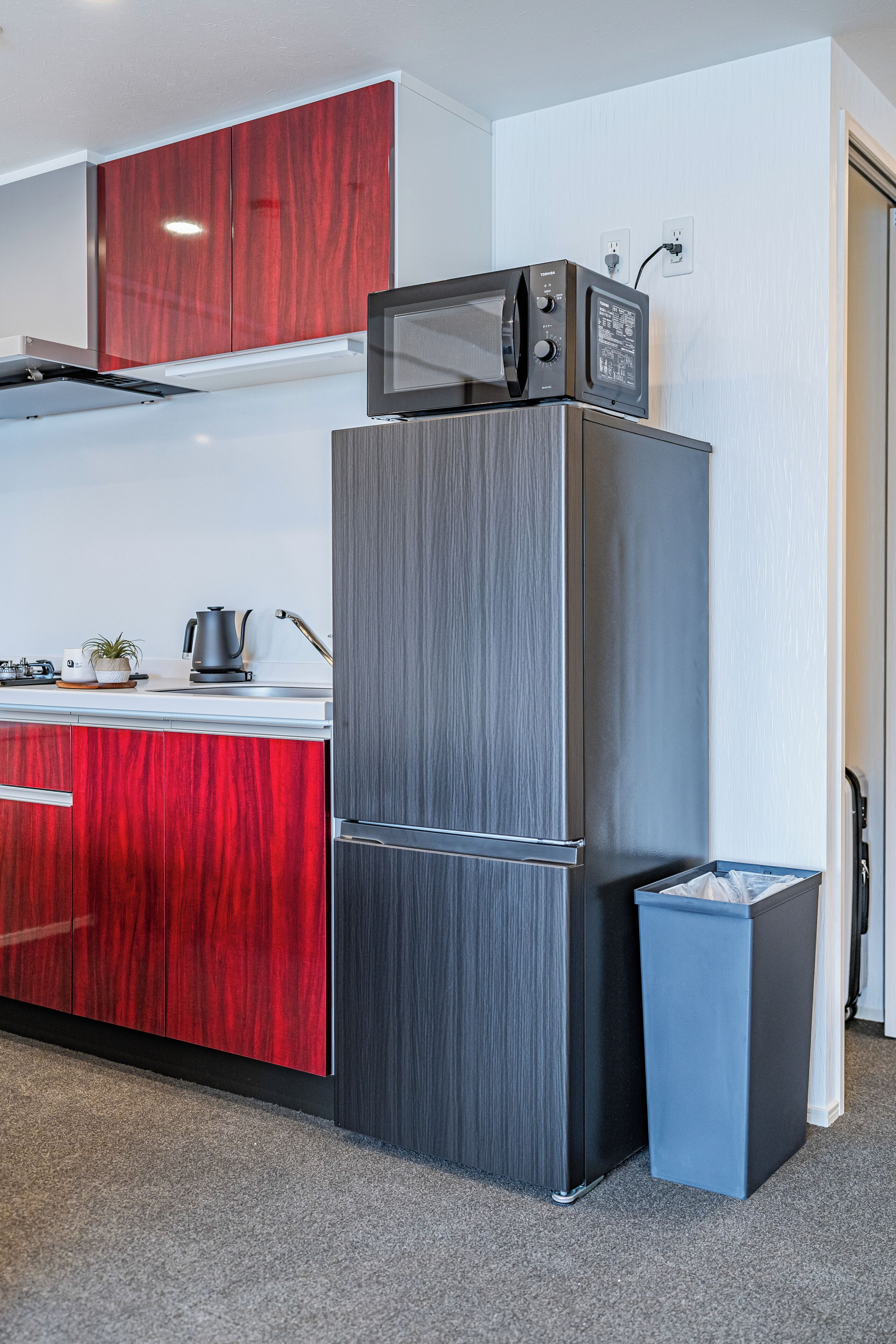 A compact kitchen with a built-in microwave, a stainless steel refrigerator, and a trash bin.