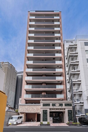 Un edificio a più piani con un design architettonico moderno, caratterizzato da balconi su ogni piano, un ingresso a livello strada e un'area di parcheggio in primo piano.
