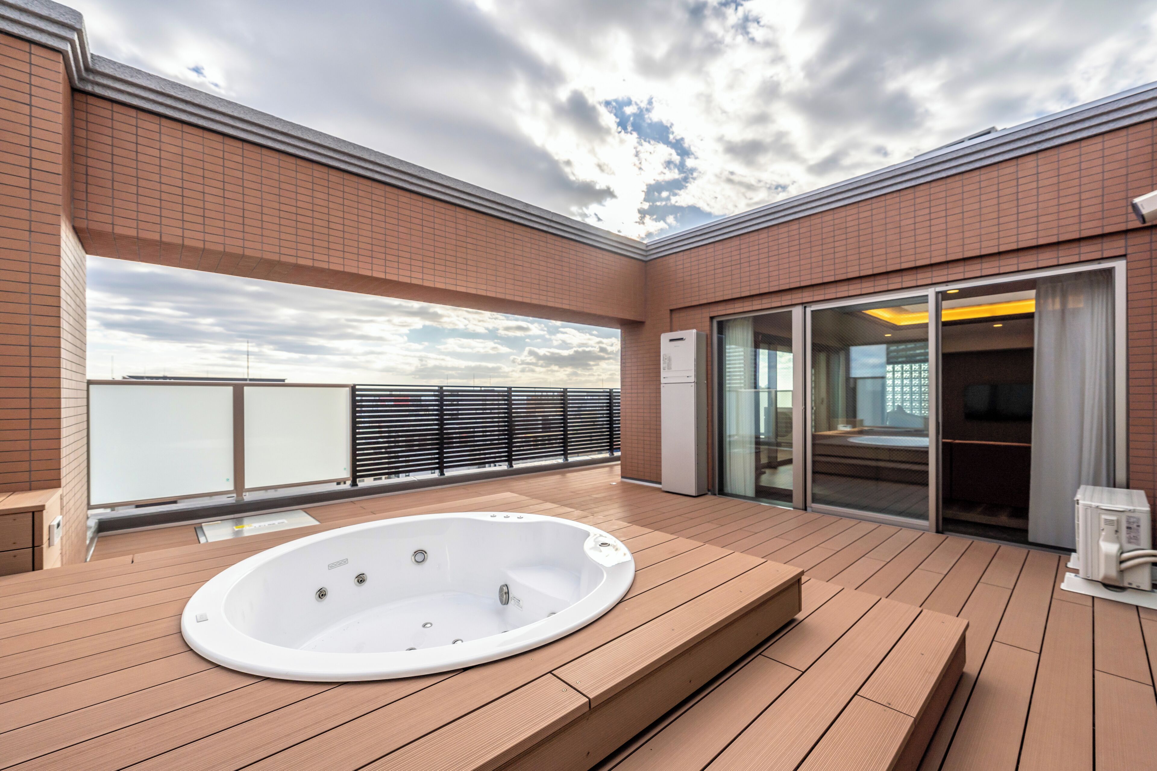 A rooftop terrace with a hot tub, wooden deck, and a glass door leading to an indoor area.