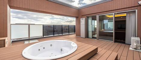 A rooftop terrace with a hot tub, wooden deck, and a glass door leading to an indoor area.