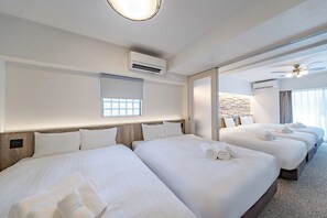 Ein Hotelzimmer mit drei Betten, einer Klimaanlage, einem Fenster mit Jalousien und einem Deckenventilator.