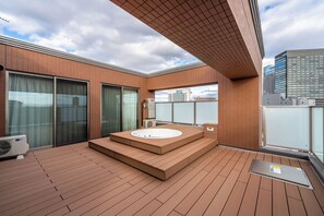 A modern outdoor hot tub area with a wooden deck, a large window, and a view of the city skyline. - Apartment Hotel 11 Namba Motomachi (Osaka)