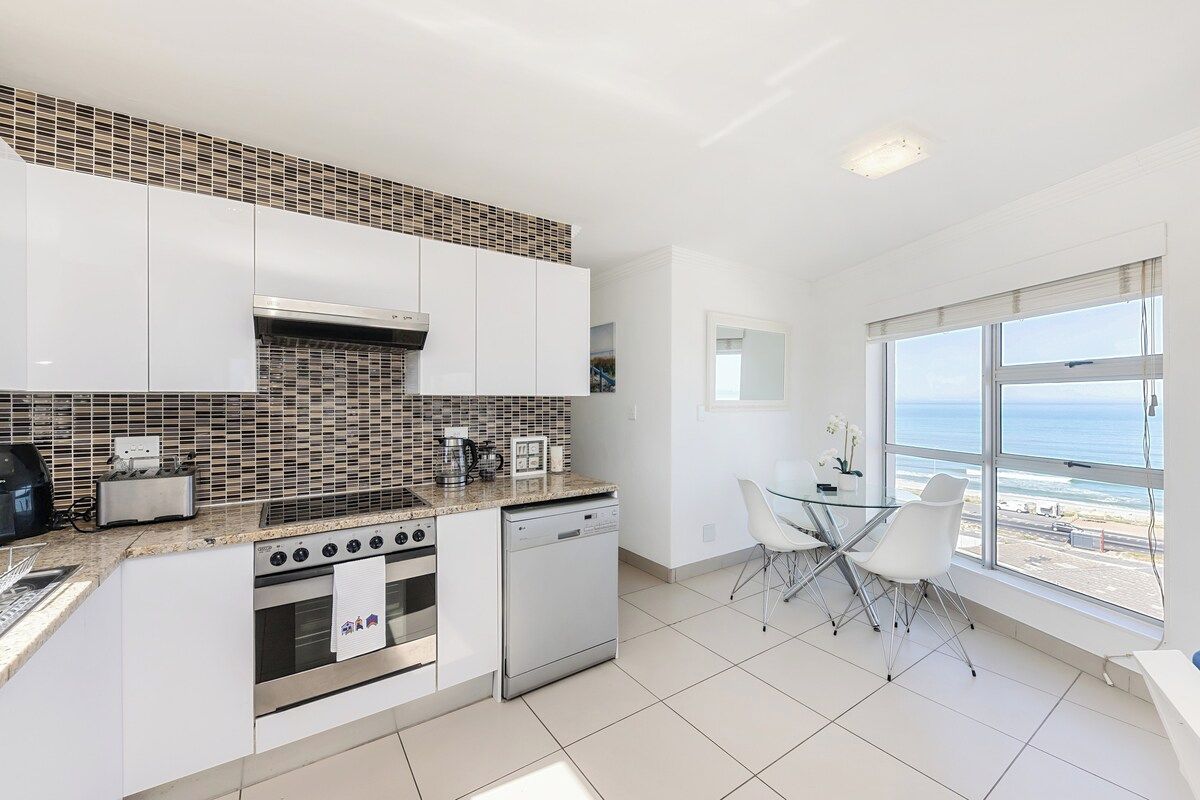 A modern kitchen with white cabinets, a tiled backsplash, and a view of the ocean through large windows.
