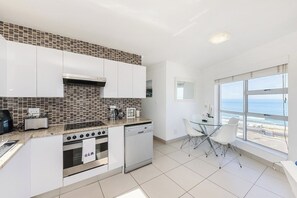 A modern kitchen with white cabinets, a tiled backsplash, and a view of the ocean through large windows.