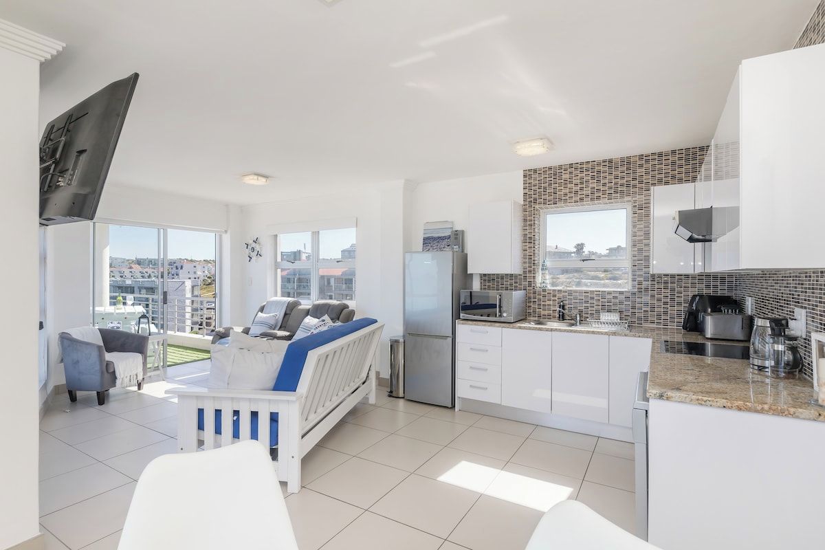 A modern apartment with a living area, kitchenette, and a balcony with a city view.