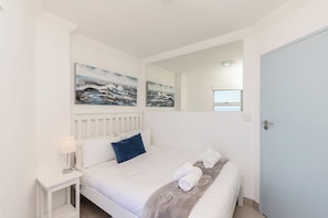 A hotel room with a bed, a nightstand, a lamp, a mirror, and artwork on the wall. - Blouberg Beauty Sea & Table mountain views (Milnerton)