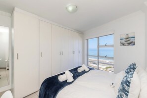 A bedroom with a bed, a large window with a view of the sea, and a wardrobe. - Blouberg Beauty Sea & Table mountain views (Milnerton)