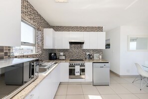 A modern kitchen with white cabinets, a built-in oven, a dishwasher, and a window providing natural light.