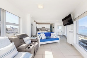 A modern living room with a sofa, a television, and a view of the sea. - Blouberg Beauty Sea & Table mountain views (Milnerton)