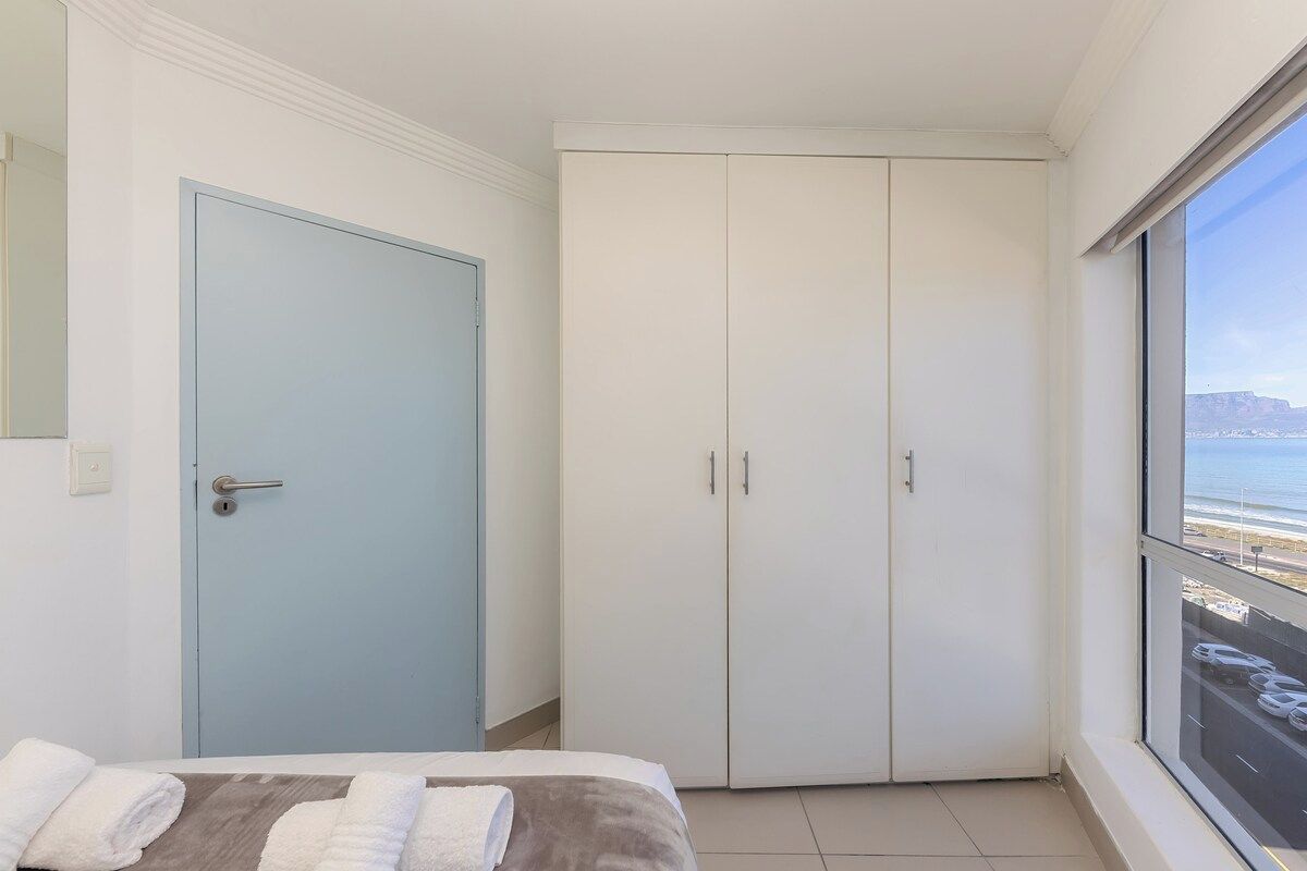 A bedroom with a bed, a wardrobe, and a window with a view of the sea.