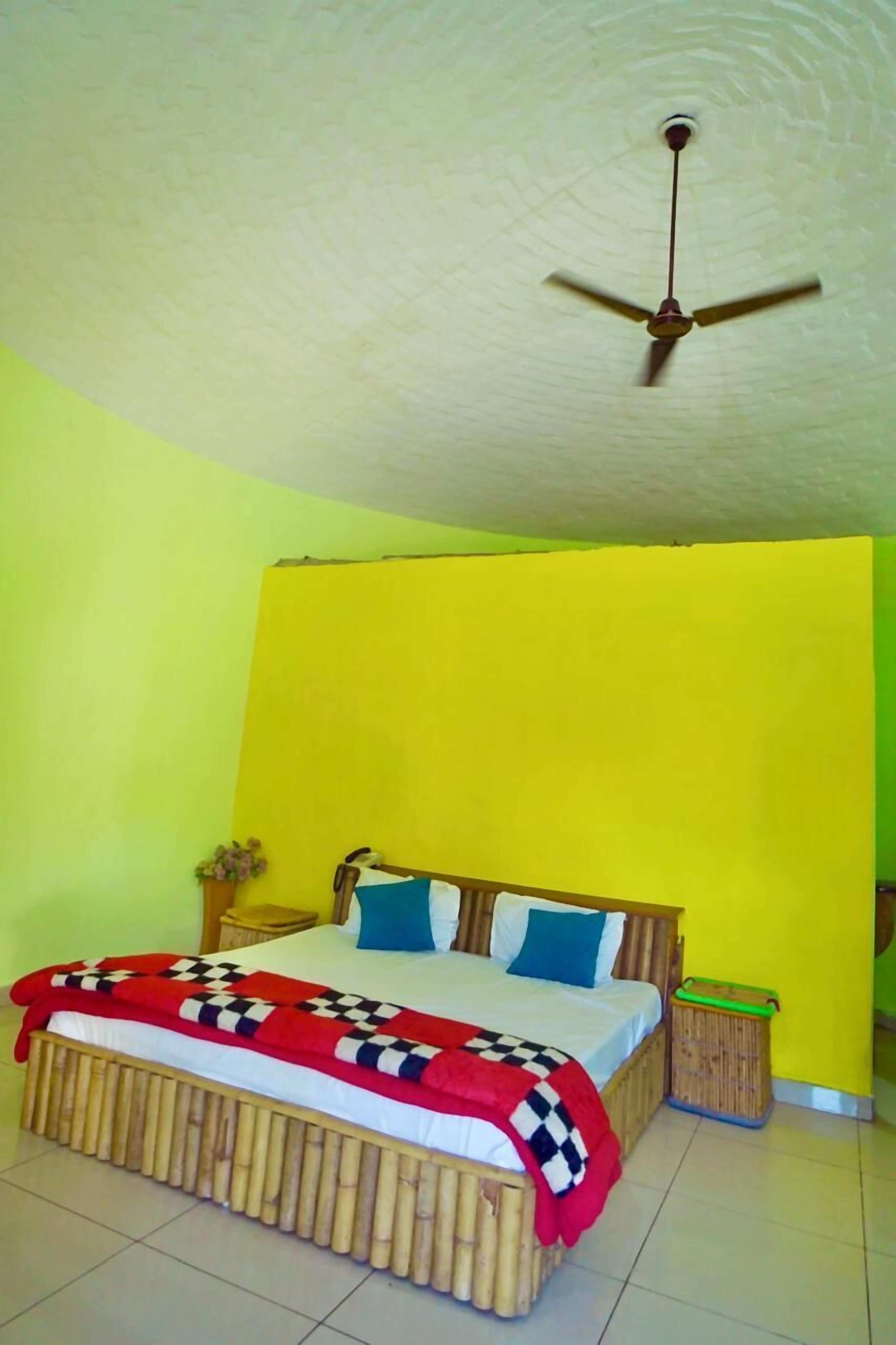 A room with a bed, a ceiling fan, a nightstand, and a trash bin.