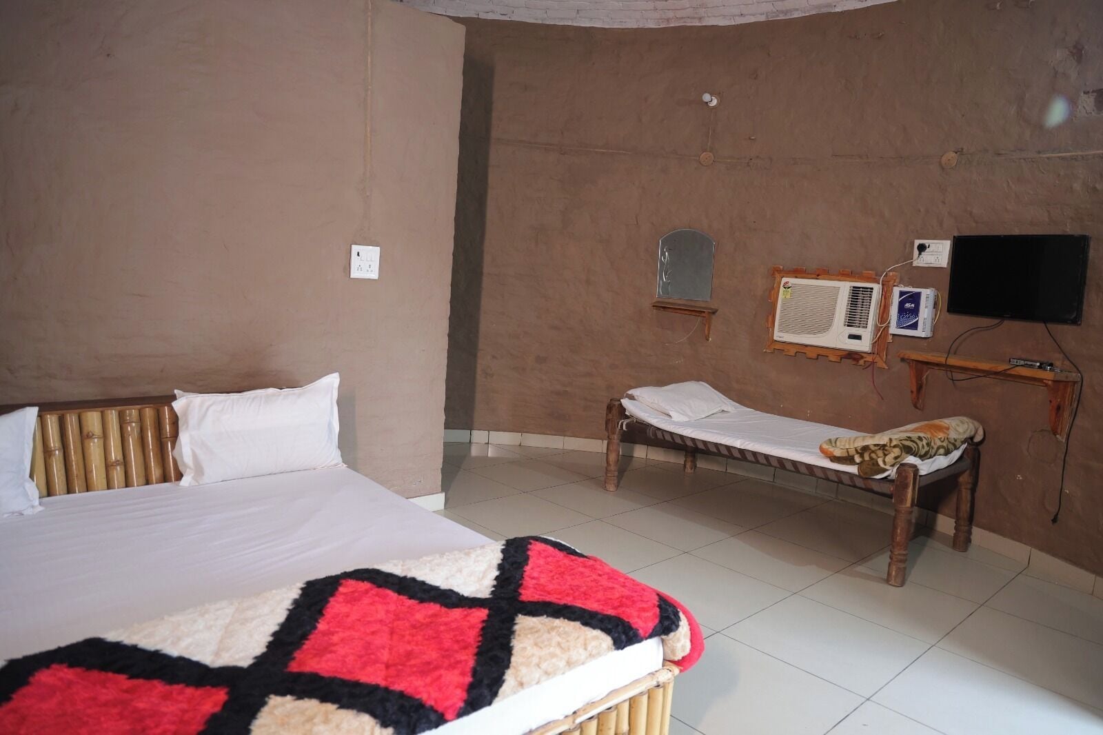 A bedroom with a bed, a bench, a television, and an air conditioning unit.