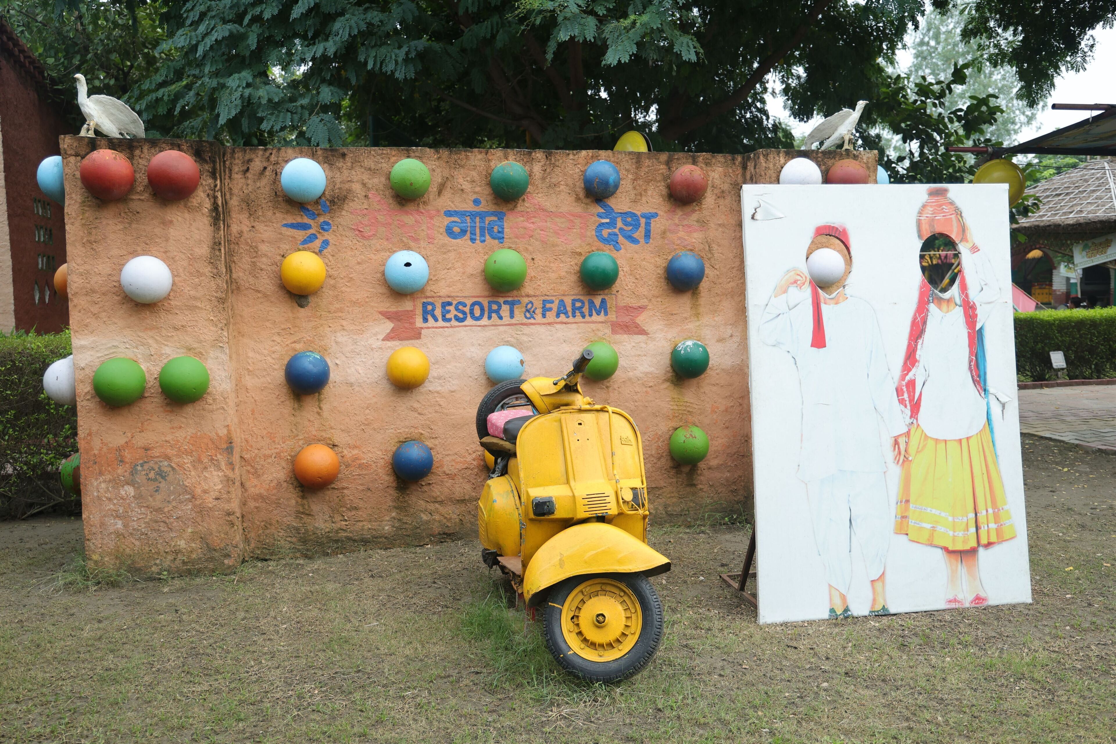 Uma scooter amarela estacionada em frente a uma parede com bolas coloridas e uma pintura de duas figuras.