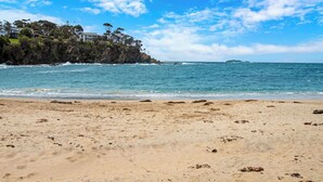 Ein Strand mit klarem, blauem Wasser, einem sandigen Ufer und einer felsigen Klippe mit Häusern.