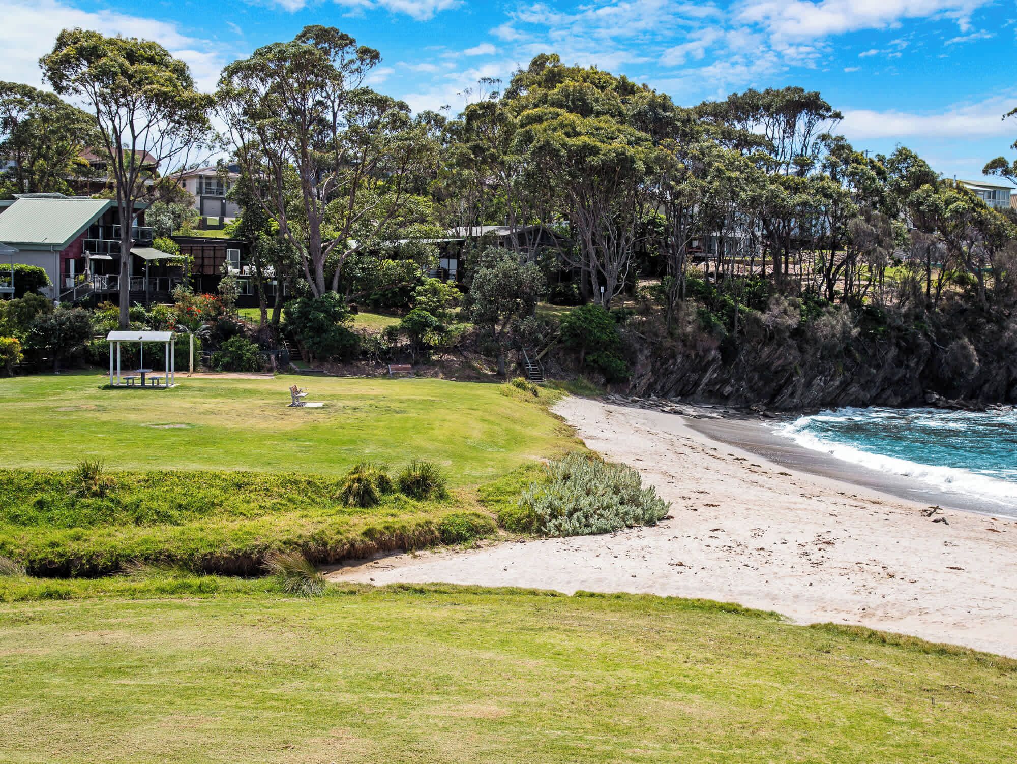A coastal property with a grassy lawn, a white gazebo, and a beach.