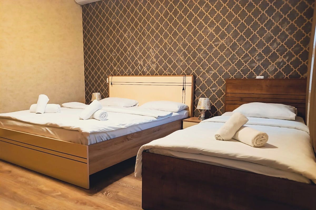 Deux lits en bois avec du linge de lit et des serviettes blanches, un mur décoré d’un motif et un plancher en bois.