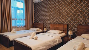 A hotel room with two beds, a window with curtains, an air conditioning unit, and patterned wallpaper.