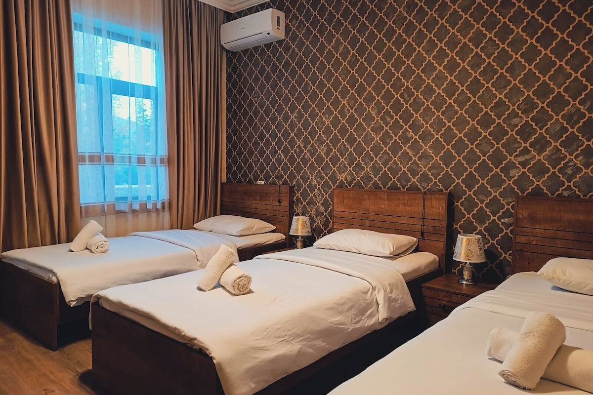 Une chambre d’hôtel avec deux lits, une fenêtre avec des rideaux, un appareil de climatisation et un papier peint à motifs.