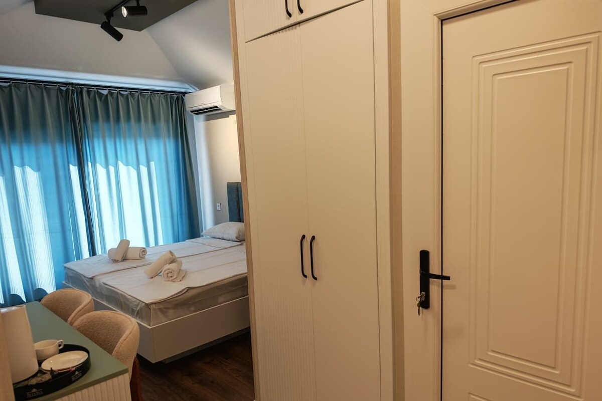 A hotel room with a bed, a desk with a chair, a wardrobe, and a door.