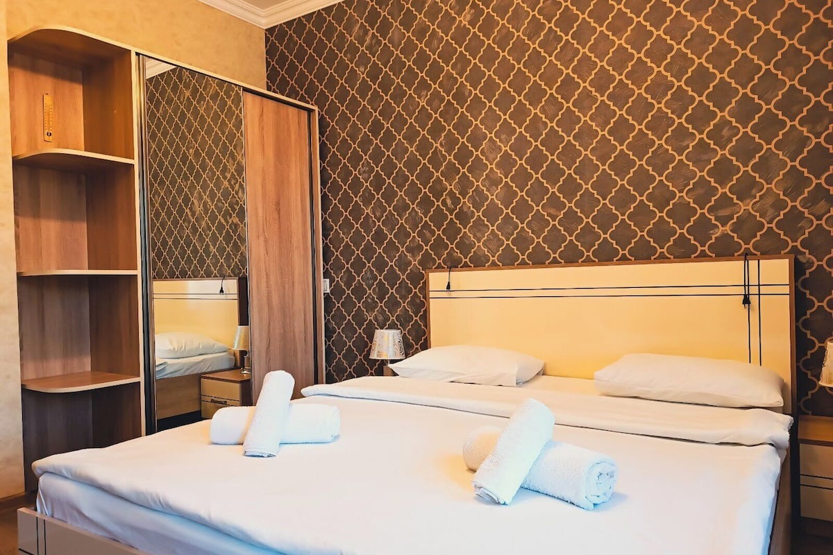 Une chambre d’hôtel avec un lit, deux tables de chevet, une armoire et un mur décoré d’un motif.