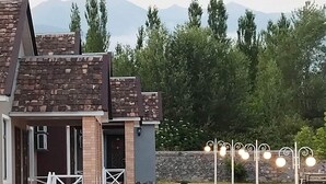 A modern building with a brick facade, a stone wall, and a paved walkway leading to a seating area with string lights. - Tulpan Hotel (Sheki)